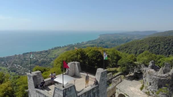 Vista aérea da torre de defesa. A fortaleza de pedra branca está localizada no topo da montanha. É iluminado pela luz solar brilhante. Você pode ver estrada serpentina e cume caucasiano na distância — Vídeo de Stock