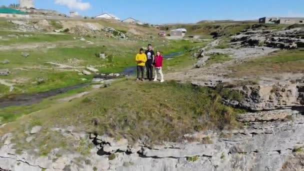 Vista aérea de una cascada alta en Daguestán. El agua corre por el acantilado a la luz del sol. La meseta de piedra está cubierta de vegetación y carreteras donde los coches conducen. Reflejos de arco iris del agua — Vídeos de Stock