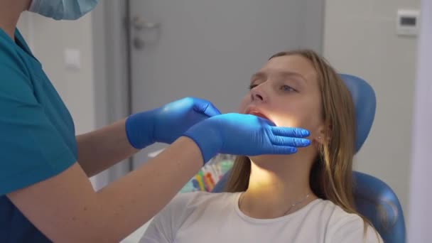 De orthodontist voelt zijn tanden met zijn vingers. Een gemaskerde dokter controleert het resultaat van zijn werk. De dokter draagt rubberen handschoenen aan zijn handen. De mond van de patiënten is wijd open. Beugels — Stockvideo