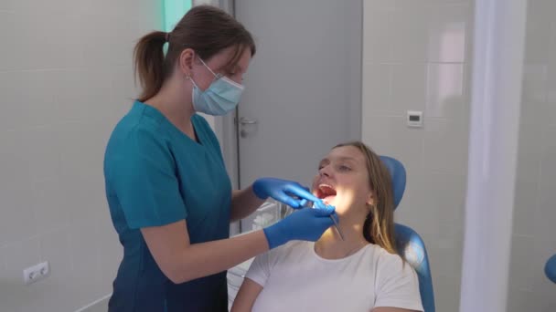 O ortodontista retira a banda elástica rosa de aparelhos com a ferramenta. As mãos dos médicos estão em luvas de borracha. A boca dos pacientes está bem aberta. A mulher está feliz com o resultado. Aparelhos — Vídeo de Stock