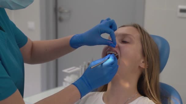 A fogszabályozó szerszámokkal rögzíti a gumiszalagokat a fogszabályzón. Az orvosok kezei gumikesztyűben vannak. A betegek szája tárva-nyitva. A nő elégedett az eredménnyel, és széles körben mosolyog. Fogszabályzó — Stock videók