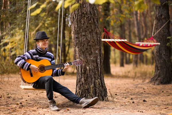 Joven Guapo Atractivo Hombre Suéter Tocando Guitarra Bosque Sentado Columpio — Foto de Stock