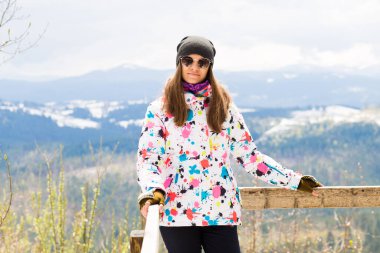 Renkli ceketli mutlu turist kız baharın erken saatlerinde karla kaplı dağlarda gözlem güvertesinde duruyor.