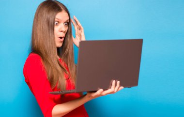 Kırmızı elbiseli genç kızın portresi dizüstü bilgisayarla mavi arka planda izole edilmiş.