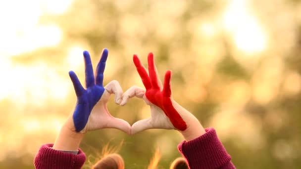 Love and happiness concept. Cute child forming heart gesture with hands outdoors on nature sunset bokeh background. Heart shape of kids hand painted in france flag colors, childrens love concept.
