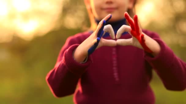 Koncepcja miłości i szczęścia. Cute dziecko tworzące gest serca z rąk na zewnątrz na natura zachód słońca bokeh tle. Kształt serca dzieci ręcznie malowane we francuskich kolorach flagi, dzieci koncepcji miłości. — Wideo stockowe