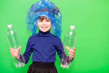 Kızın elinde çöp torbası ve plastik şişe var ve yeşil arka planda izole edilmiş çevresel sorunlarla ilgilendiğini gösteriyor. Çocukluktan beri çöplerin sorumluluğunu taşımaya alışkın bir çocuk..