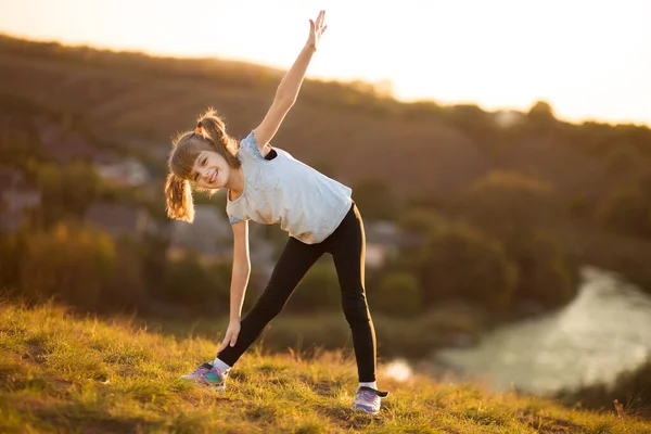 Liten flicka gör sport övningar vid solnedgången — Stockfoto