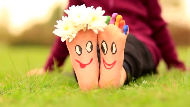 Klein kind meisje zit op gras met geschilderde voeten met grappige komische gezichten — Stockvideo