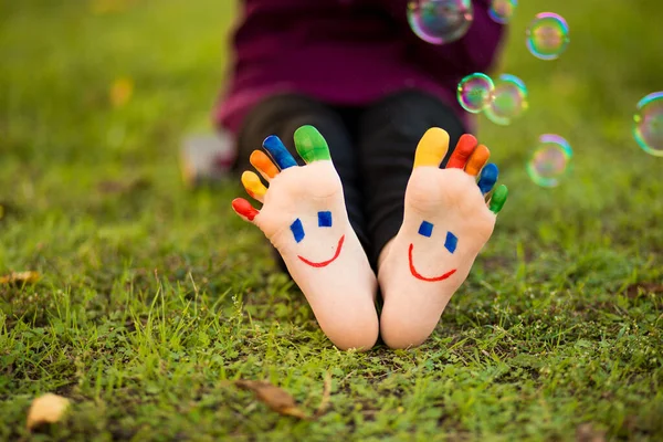 Παιδικά πόδια με τη ζωγραφική χαμόγελα που βρίσκονται στο πράσινο γρασίδι — Φωτογραφία Αρχείου