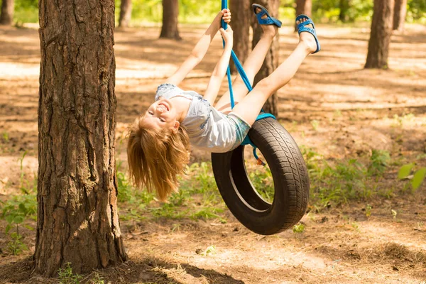 Cute little girl swinging na kole dołączony do dużego drzewa w lesie. — Zdjęcie stockowe