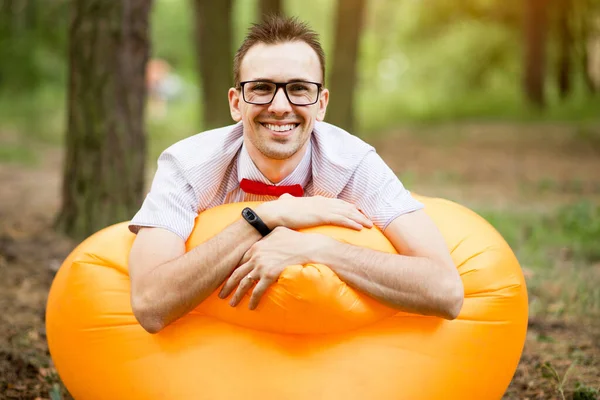 Kjekk ung mann i briller som ligger på oppblåsbar gul sofa og hviler i parken – stockfoto