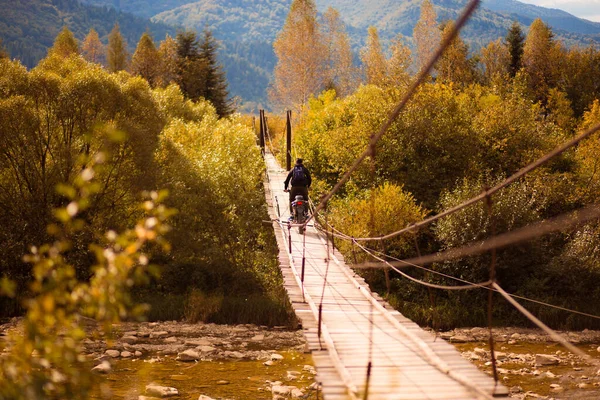 Unbekannter Mann läuft mit Cross-Country-Motorrad auf Hängebrücke über Gebirgsfluss — Stockfoto