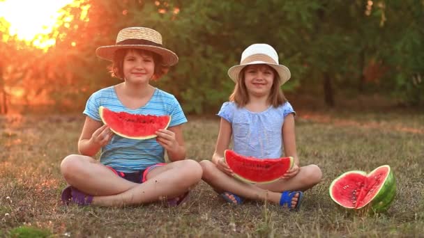 Två förskolor ler barnsyster äter vattenmelon i sommarparken med solnedgång — Stockvideo