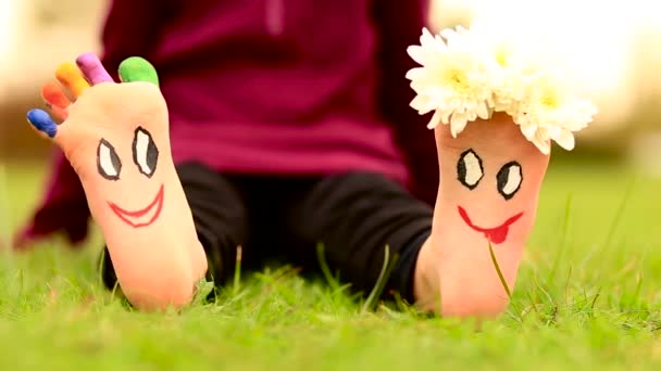 Klein kind meisje zit op gras met geschilderde voeten met grappige komische gezichten — Stockvideo
