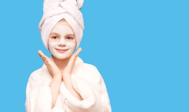 Kafasına havlu sarılmış mutlu çocuk ifadesi mavi üzerine izole edilmiş, yüzüne doğal güzellik ürünü sürmüş, gözenekleri açmış, sağlıklı cilt.