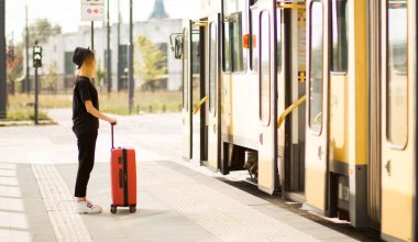 Şık bir kadın tamamen siyah ve kırmızı valizli durak bekleyen bir tramvay bekliyor.