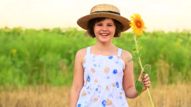 Ay çiçeği tutan ve yaz tarlasında gülen sevimli mutlu kız. Güzel, neşeli genç kız, sarı ayçiçekleri arasında poz veriyor.