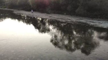 Genç bir kadının hava aracı görüntüsü yaz sabahı dağlarda nehir boyunca yürüyor.