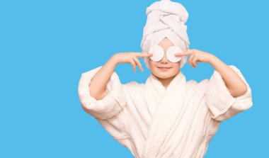 Kafasında havluyla gülümseyen güzel bir kız çocuğu pamuk tutacağı ile cildi temizleyici ile temizliyor. Mutlu kız makyajını temizler sağlıklı cilt bakımının tadını çıkarır.