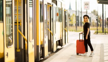 Tam boy seyahat portresi. Siyah giyinmiş, kırmızı valizli genç bir kadın.