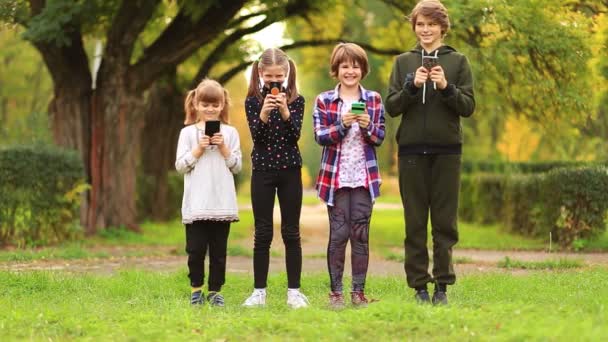 Happy children friend girls group walk together in summer park and playing internet game with mobile smartphone. kids texting message on phone outdoor in summer garden. Blogger lifestyle — Stock Video