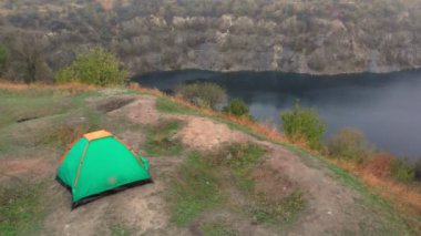 Aktif aile seyahati kavramı. Küçük kızlarıyla birlikte göl kenarında yürürken ellerini kaldırarak kamp çadırında yürüyen genç ebeveynlerin hava görüntüsü.. 