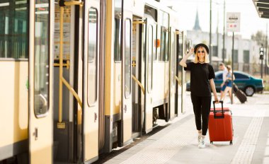 Tam boy seyahat portresi. Siyah giyinmiş, kırmızı valizli genç bir kadın.