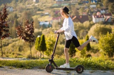 Beyazlı genç sarışın kadın yazın elektrikli scooterla işe gidiyor..
