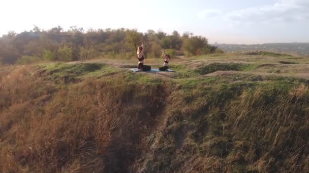 Luchtfoto drone uitzicht van slanke jonge moeder doen yoga oefeningen met kind dochter op hoge heuvel door meer in de ochtend, ver van drukte van de stad, goed voorbeeld en inboezemen in haar gezonde gewoonten — Stockvideo