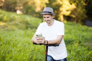 Şapkalı genç adam cep telefonu kullanıyor, internetten elektrikli scooter kiralıyor. Yenilikçi ulaşım