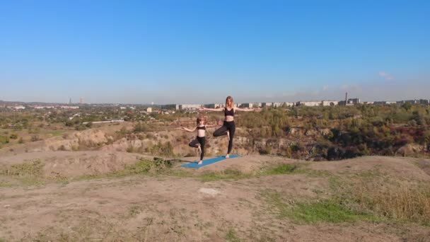 Veduta aerea drone di snella giovane madre fare esercizi di yoga con figlia bambino in alta collina sul lago al mattino, lontano dal trambusto della città, dare il buon esempio e instillare nelle sue abitudini sane — Video Stock