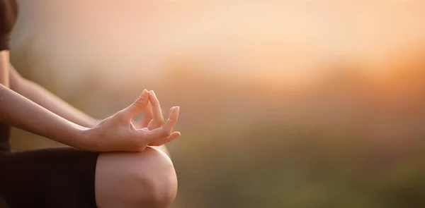 Close up with selective focus of hands woman sitting in yoga lotus pose outdoor at sunrise, meditating for balance. Horizontal banner view for website header design with copy space — Stock Photo, Image