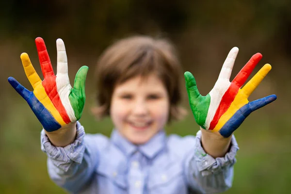 Vrolijk meisje tonen hallo gebaar met de handen geschilderd in regenboog kleuren. Focus op handen — Stockfoto