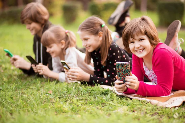 Arkadaşlarıyla dışarıda telefonla oynayan küçük bir kızın açık hava portresi. 