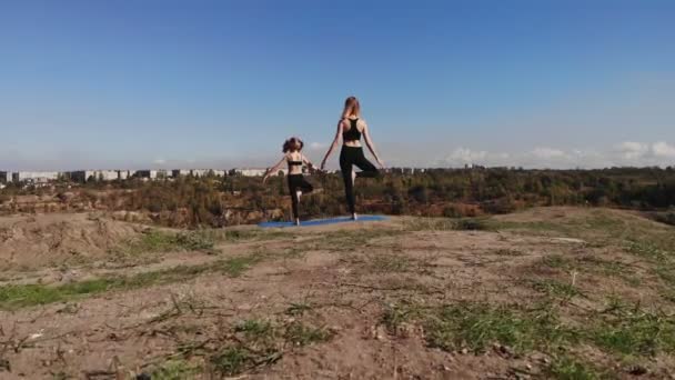 Mince jeune mère faire des exercices de yoga avec fille enfant sur la haute colline au bord du lac le matin, loin de l'agitation de la ville, donner le bon exemple et inculquer ses saines habitudes — Video