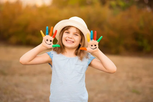Счастливая улыбающаяся маленькая девочка с руками в красках играет под открытым небом в парке — стоковое фото