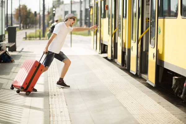 Jeune voyageur coiffé d'un chapeau avec une valise qui roule en gare. Tourisme en retard sur le voyage en avion — Photo
