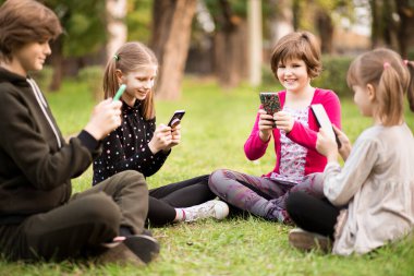 Arkadaşlarıyla dışarıda telefonla oynayan küçük bir kızın açık hava portresi. 