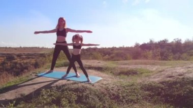 İnce ve genç annenin hava drone görüntüsü, sabahları kızıyla birlikte yüksek tepelerde, göl kenarında yoga egzersizleri yapıyor. Şehrin çalkantısından uzakta, iyi örnek oluyor ve sağlıklı alışkanlıklarını ona aşılıyor.