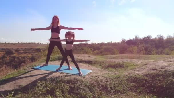 Aerial drone widok smukłej młodej matki ćwiczyć jogę z córką na wysokim wzgórzu nad jeziorem rano, z dala od zgiełku miasta, dać dobry przykład i wpajać w jej zdrowych nawyków — Wideo stockowe