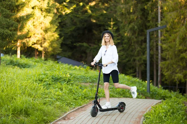 Seitenansicht der jungen blonden Frau in Weiß gehen auf Elektroroller in der Stadt Sommer arbeiten. — Stockfoto