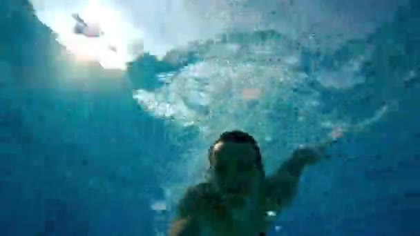 Feliz hombre activo saltando bajo el agua con los ojos abiertos en la piscina y hacer auto video en la cámara de acción. Vacaciones de verano — Vídeo de stock