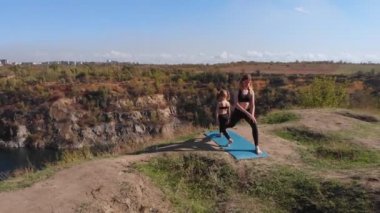 İnce ve genç annenin hava drone görüntüsü, sabahları kızıyla birlikte yüksek tepelerde, göl kenarında yoga egzersizleri yapıyor. Şehrin çalkantısından uzakta, iyi örnek oluyor ve sağlıklı alışkanlıklarını ona aşılıyor.