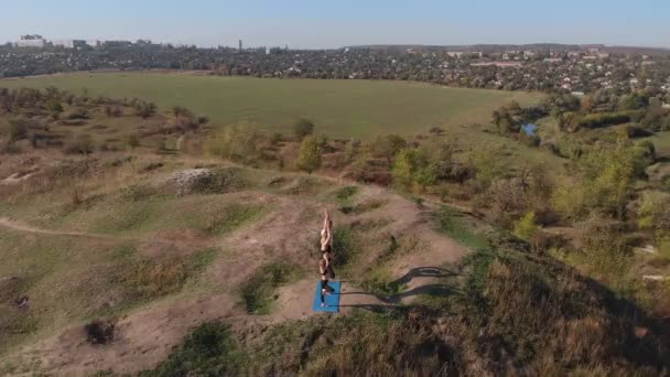 Orbitando plano aéreo de familia de tres, madre padre e hija, hacer ejercicios de yoga en la cima de la colina en la mañana soleada. Formación familiar joven lejos del bullicio de la ciudad, dar buen ejemplo e inculcar en — Vídeos de Stock