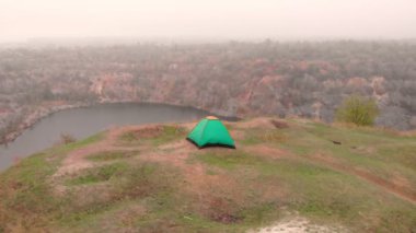 Kampta göl kenarındaki tepenin üstündeki turist çadırının hava görüntüsü. Kamp yaparken dışarıda dinleniyor. Yazın ormanlık alanda güzel bir doğa yeri.