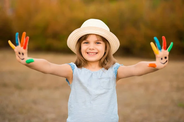 Feliz niña sonriente con las manos pintadas en la cara divertida jugar al aire libre en el parque. —  Fotos de Stock