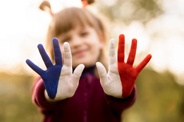 Joyful girl waving hands painted in France flag colors and say hello outdoor at sunset