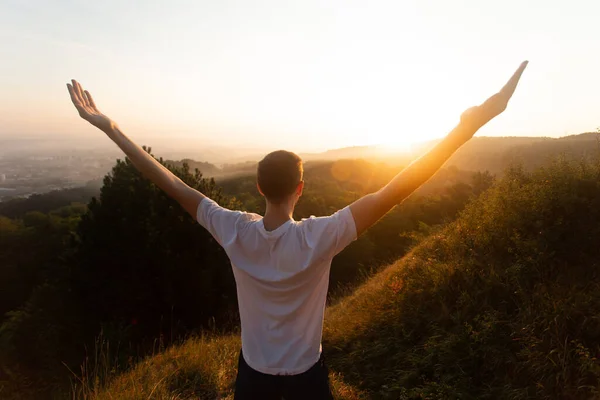 Silhouette di giovane uomo alza le mani fino al tramonto o all'alba sulla cima della collina in estate — Foto Stock