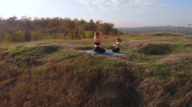 İnce ve genç bir annenin hava aracı görüntüsü, sabah kızıyla birlikte yüksek tepelerde yoga egzersizleri yapıyor, şehrin telaşlı ortamından uzakta, iyi örnek oluyor ve sağlıklı alışkanlıklarını ona aşılıyor.